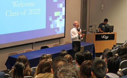 Guglielmo speaks to an auditorium behind a screen that reads 'Welcome Class of 2022!'