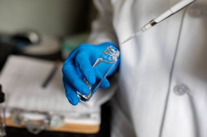 gloved hands hold a pipette to a vial.