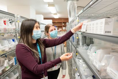 Yang and Kaip inspect small boxes of medicine on a storage rack