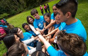 Students at Golden Gate Park, wearing Orientation t-shirts, clasping their overlapping hands in a circle