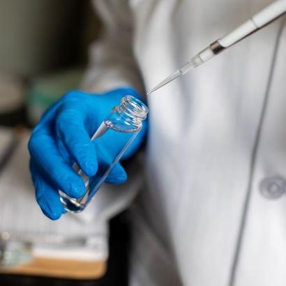 gloved hands hold a pipette to a vial.