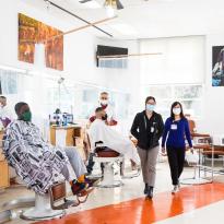 Two pharmacists walking past two barbers and their clients in a barbershop