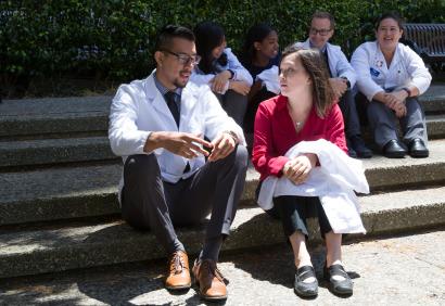 Small group of PharmD students in white coats, sitting on steps