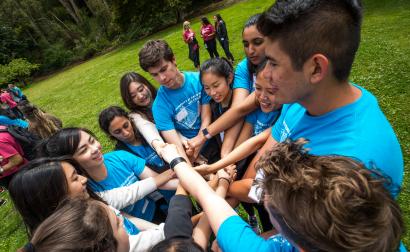 Students at Golden Gate Park, wearing Orientation t-shirts, clasping their overlapping hands in a circle