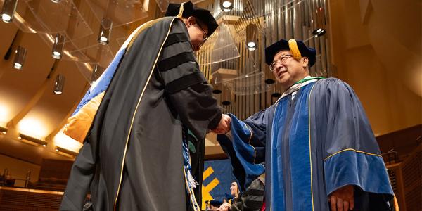 Brian Komoto shakes the hand of a graduate at commencement