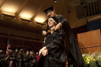 Kearney places a graduation hood on a student on stage
