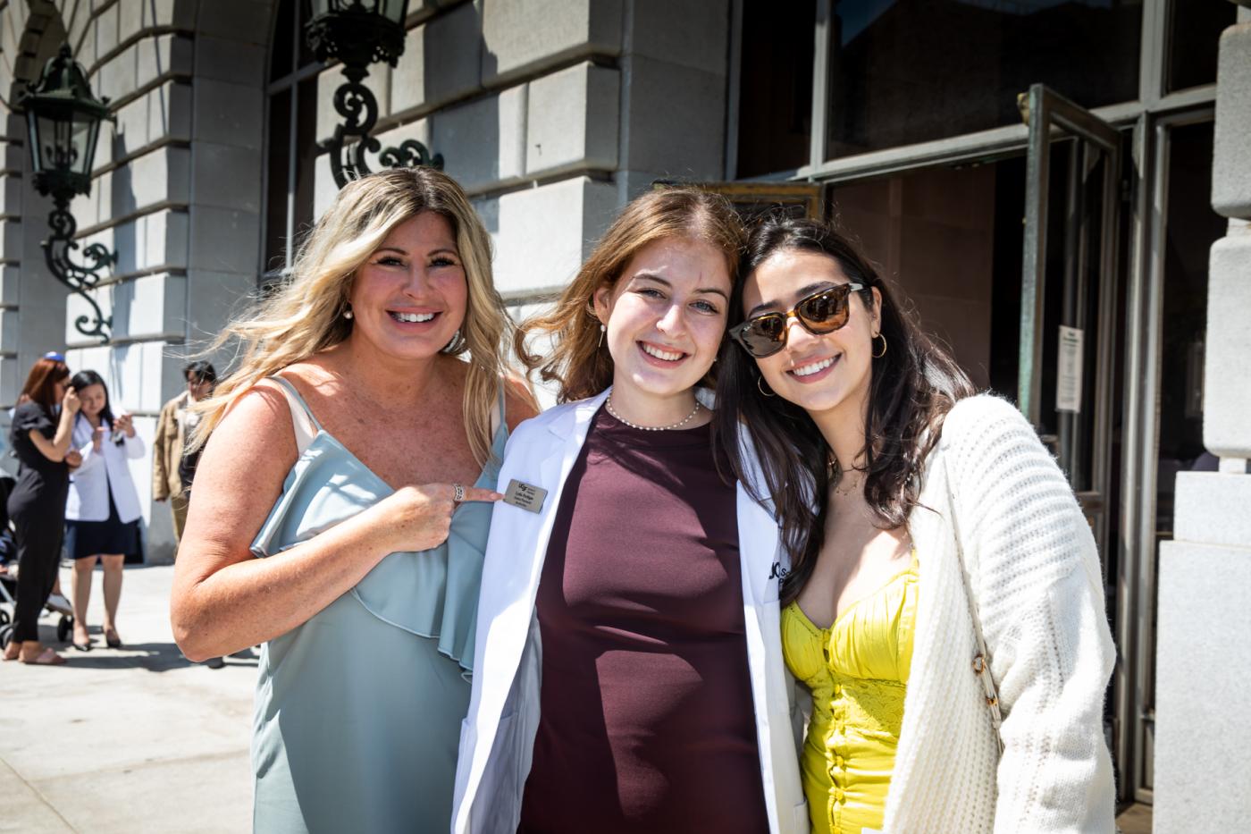 Three women, the middle wearing white coat, left pointing at PharmD nametag.